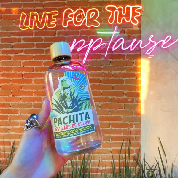 Botella de destilado de pulque con un fondo que dice Live for the applause 