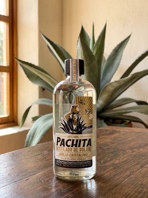 Botella de destilado de pulque Pachita Añejo Cristalino 37°, 750 mL, sobre mesa de madera con maguey salmiana