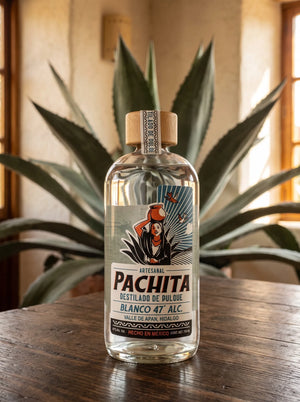 Botella de destilado de pulque Pachita Blanco 47°, 750 mL, sobre mesa de madera con maguey salmiana